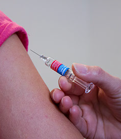 Close-up of a vaccination scene, with a seringe and a skin detail of the arm of a patient